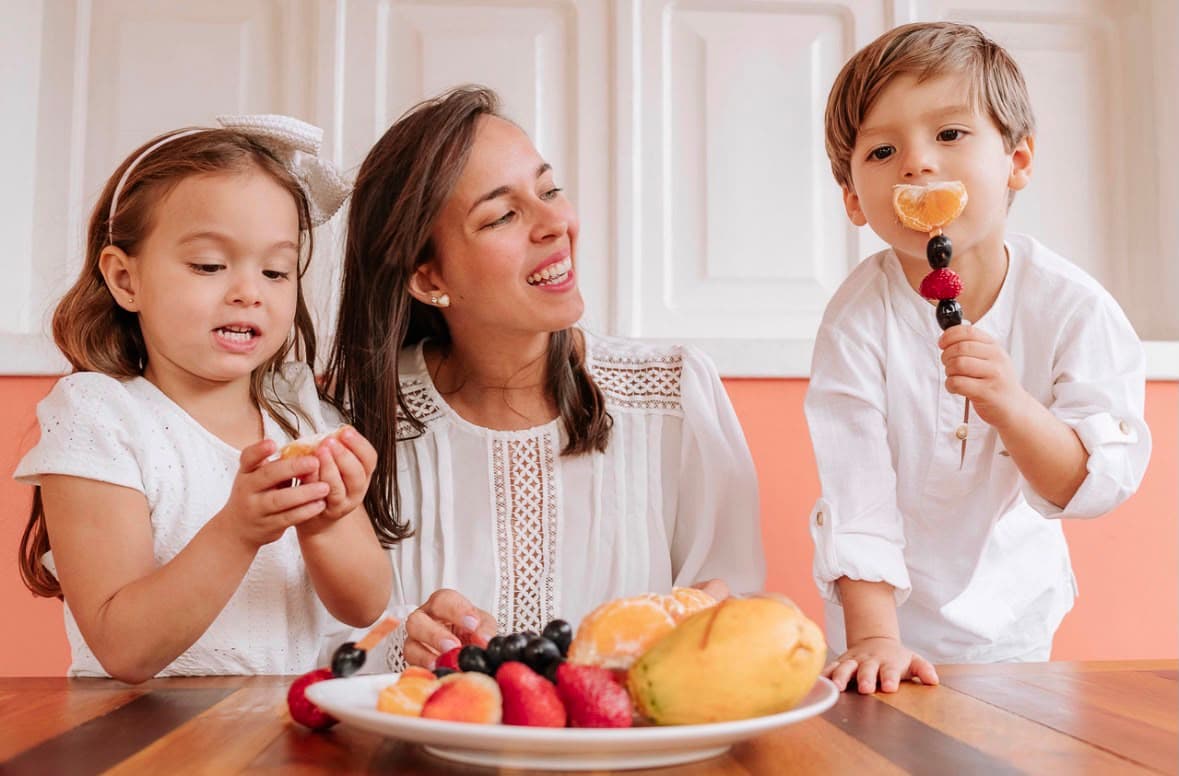 Nutricionista Camila Rios com duas crianças experimentando frutas